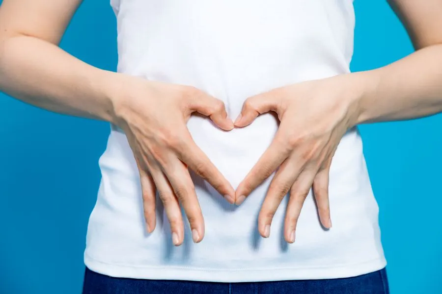 A young woman makes a heart shape with her hands on her stomach